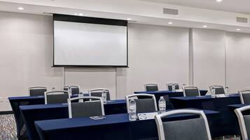 Un salón de conferencias con mesas, sillas, una pantalla de proyector y tarjetas de identificación.