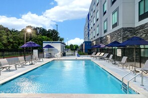 Una piscina al aire libre, sombrillas, sillones reclinables de piscina