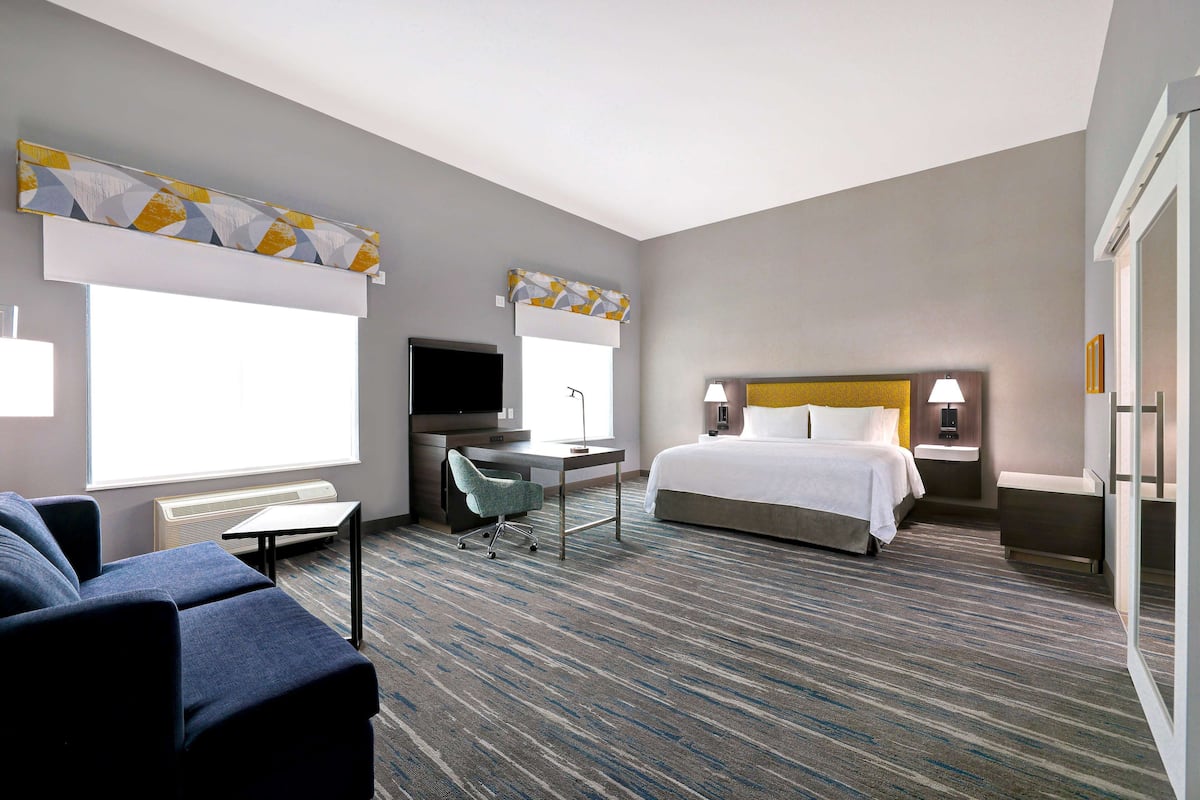 A hotel room with a bed, a desk, a chair, a TV, and a window.
