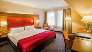 Une chambre d’hôtel avec un grand lit, deux tables de chevet avec des lampes, une chaise, une petite table ronde et une fenêtre avec des rideaux.