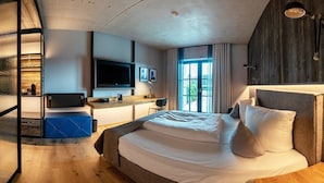 Une chambre d’hôtel moderne dotée d’un grand lit, d’un bureau, d’une télévision à écran plat et d’une grande fenêtre donnant sur l’extérieur.