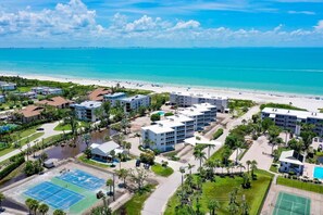 A coastal hotel with multiple buildings, a beach, and tennis courts.