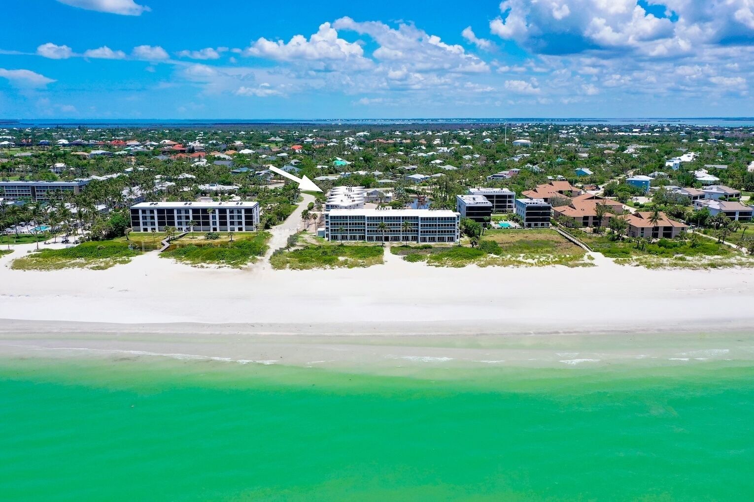 An aerial view of a coastal area with buildings, a beach, and a clear sky.