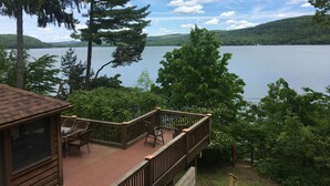 A wooden deck with outdoor furniture overlooking a lake, surrounded by trees and hills. - Pointe of View on Otsego Lake. 4 Bedrooms, 4 Bathrooms, 6 miles from Cooperstown (Cooperstown)