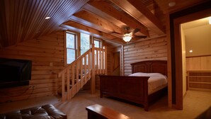 A log cabin bedroom with a wooden bed, a bench, a TV, and a staircase. - Pointe of View on Otsego Lake. 4 Bedrooms, 4 Bathrooms, 6 miles from Cooperstown (Cooperstown)
