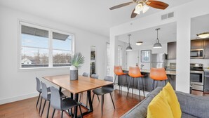 A modern kitchen with stainless steel appliances, a dining area with a wooden table and chairs, and a ceiling fan. - Chic Boutique Condo in Nashvilles coveted 12 South Neighborhood Coffee Shops, Restaurants, Bars and Boutiques, just steps away. <br>Featuring plush linens , bath products and a balcony with free parking! (Nashville)