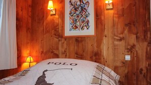 Un dormitorio con paredes de madera, una cama con almohada 'POLO' y dos lámparas fijadas a la pared.