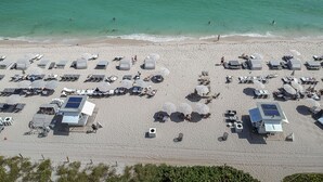 Luftaufnahme eines Strandes mit Reihen von Liegestühlen und Sonnenschirmen, einem Rettungsturm und einer Sandküste.