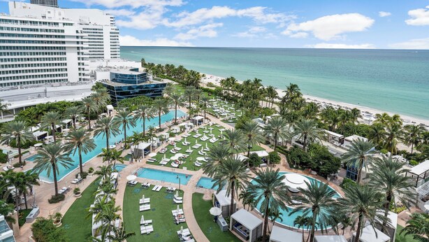 Ein Resort mit mehreren Schwimmbecken, Palmen und Blick auf den Strand.