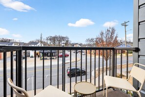 A balcony with a view of a street, a parking lot, and a building with a covered area.