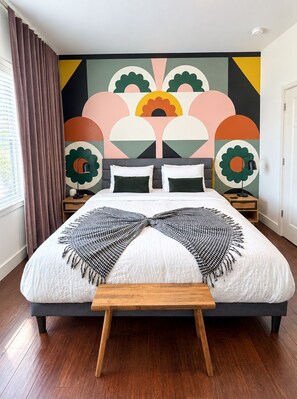 A modern bedroom with a large bed, a bench, and a colorful abstract wall art.