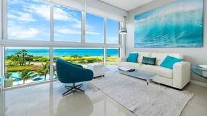 Ein geräumiges Wohnzimmer mit großem Fenster und Blick auf den Ozean und einen Strand.