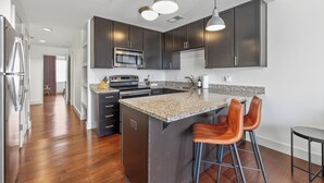 A modern kitchen with dark cabinets, a granite countertop, stainless steel appliances, and bar stools.