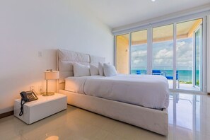 Een moderne hotelkamer met een groot bed, een bedtafeltelefoon, een lamp en uitzicht op de oceaan door grote ramen.