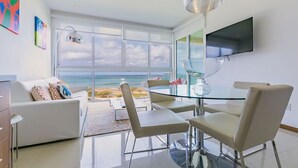 Un salon moderne avec une table en verre, des canapés blancs et une grande fenêtre donnant sur la mer.
