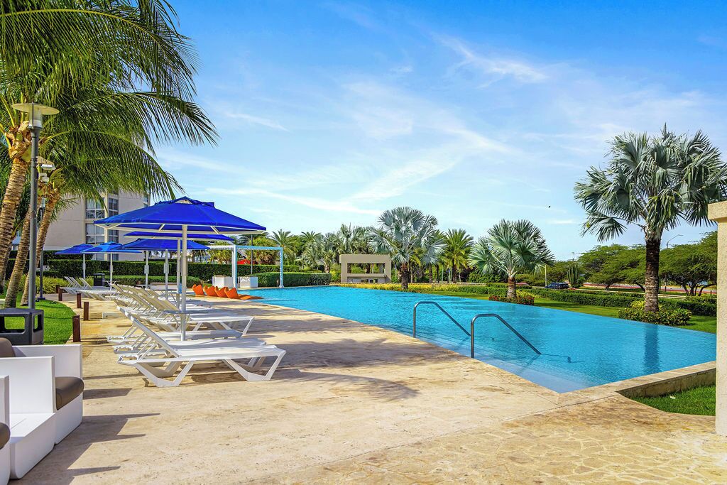 A pool area with lounge chairs, a blue umbrella, and palm trees.