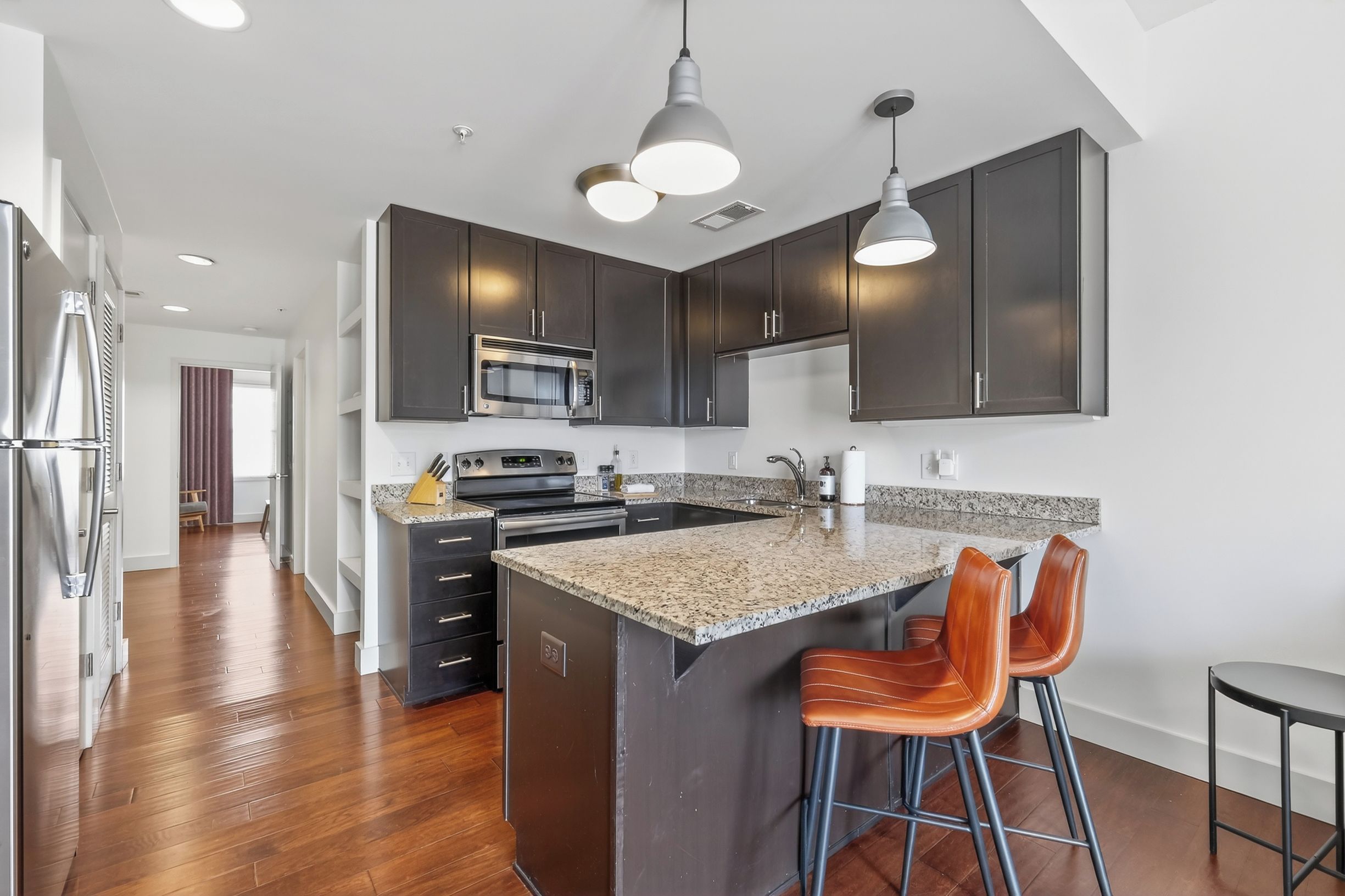 A modern kitchen with dark cabinetry, a central island with bar stools, stainless steel appliances, and pendant lighting.