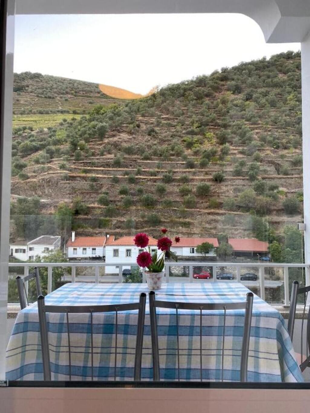 Een balkon met een eettafel, met uitzicht op een heuvel met terrassen en huizen.