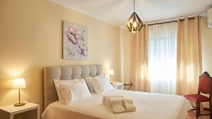A neatly made bed with white linens and pillows, a bedside lamp, and a wall-mounted painting of flowers. - Apt. in Pinhão, heart of Alto Douro wine region, vineyards and Douro River view (Pinhão)