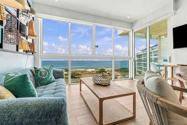 A spacious living area with a large window offering a view of the beach and ocean.