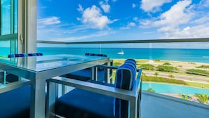 A balcony with a glass table and blue cushioned chairs, overlooking a beach and ocean. - Beach babe! An Amazing Ocean view Condo for 6. (Noord)