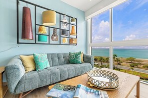 A living room with a grey sofa, a coffee table, and a view of the ocean.