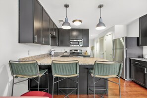 A modern kitchen with dark cabinets, a central island with bar stools, stainless steel appliances, and pendant lighting. - Coffee Shops, Restaurants, Bars,  and Boutiques, just steps away , FREE parking each unit has a balcony overlooking 12 south. (Nashville)