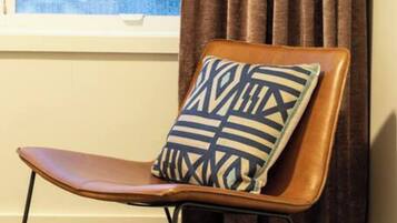 A chair with a patterned pillow, a window with curtains, and a patterned rug.