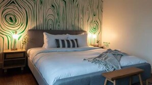 Une chambre à coucher avec un lit, des tables de chevet, un banc et un mur décoré d’un motif.