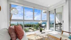 A modern living room with a large window overlooking a scenic view, a round coffee table, and a comfortable seating area. - A Boho Chic Oceanfront Condo for 6. (Noord)