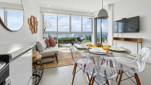 A modern kitchen with a dining area, large windows, and a TV mounted on the wall. - A Boho Chic Oceanfront Condo for 6. (Noord)