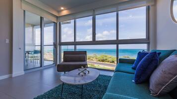 Una sala de estar moderna con un ventanal que da a una playa, un sofá, un sillón y una mesita.