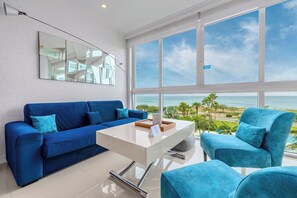 A modern living room with a blue sofa, a white coffee table, and a view of the ocean.