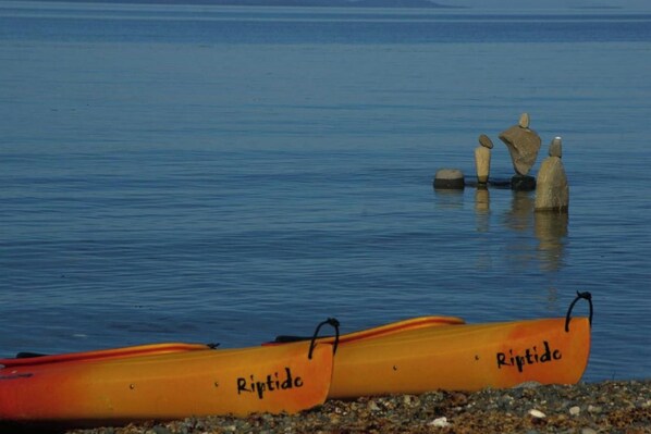 Two yellow kayaks with 'Riptide' written on them, resting on a pebbly shore by calm water.