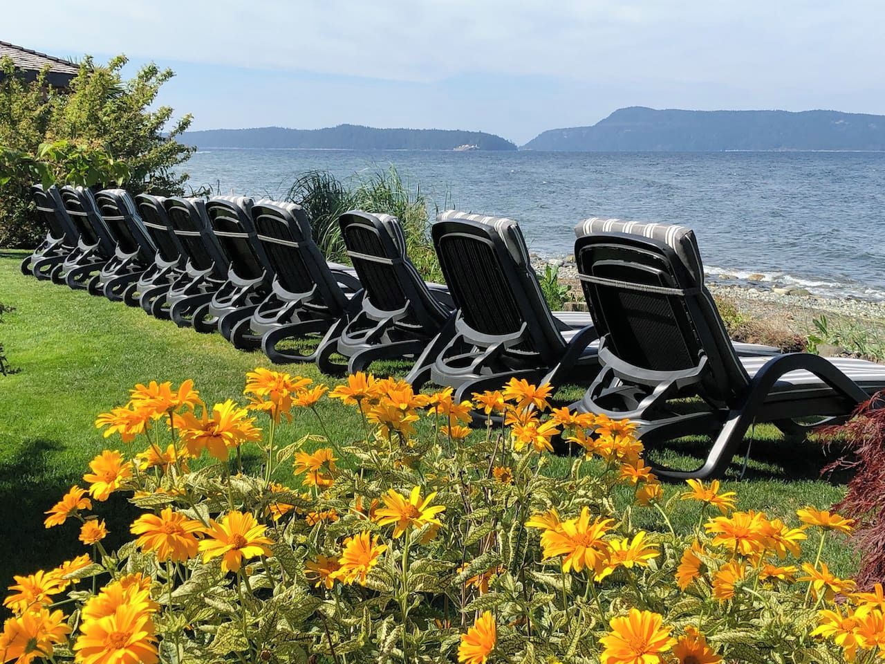 Une rangée de chaises longues est disposée face à un plan d’eau, avec des montagnes qui se dessinent à l’horizon.