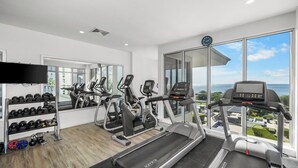 A modern gym with treadmills, elliptical machines, and a weight rack. - Beach and being Happy in one place, 1BDR condo (Eagle Beach)