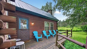 Eine Blockhütte mit einer Holzdielen-Terrasse, Sitzgelegenheiten im Freien und einer natürlichen Umgebung.