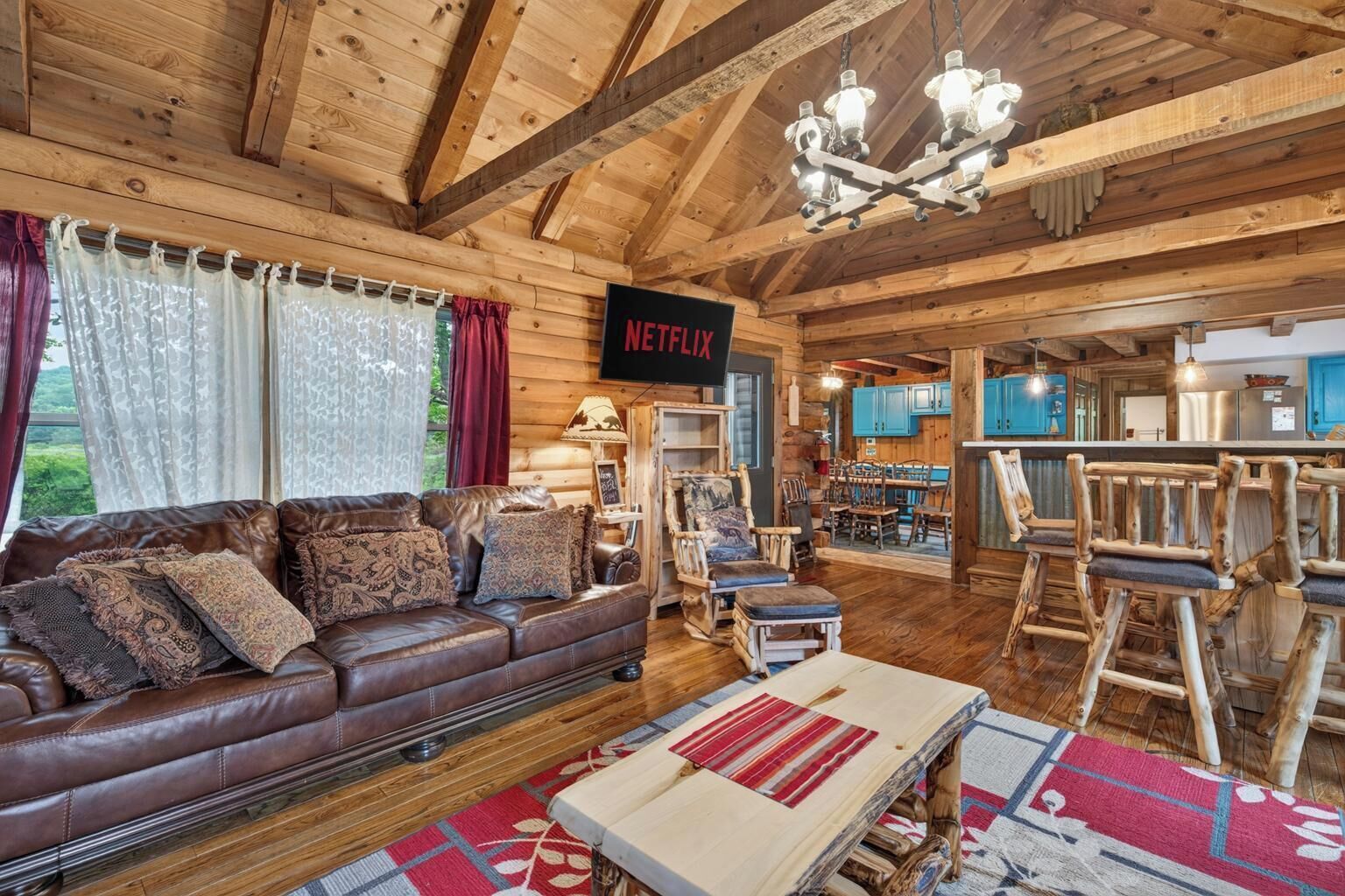 A cozy log cabin interior with a leather sofa, wooden dining table, and a bar area.