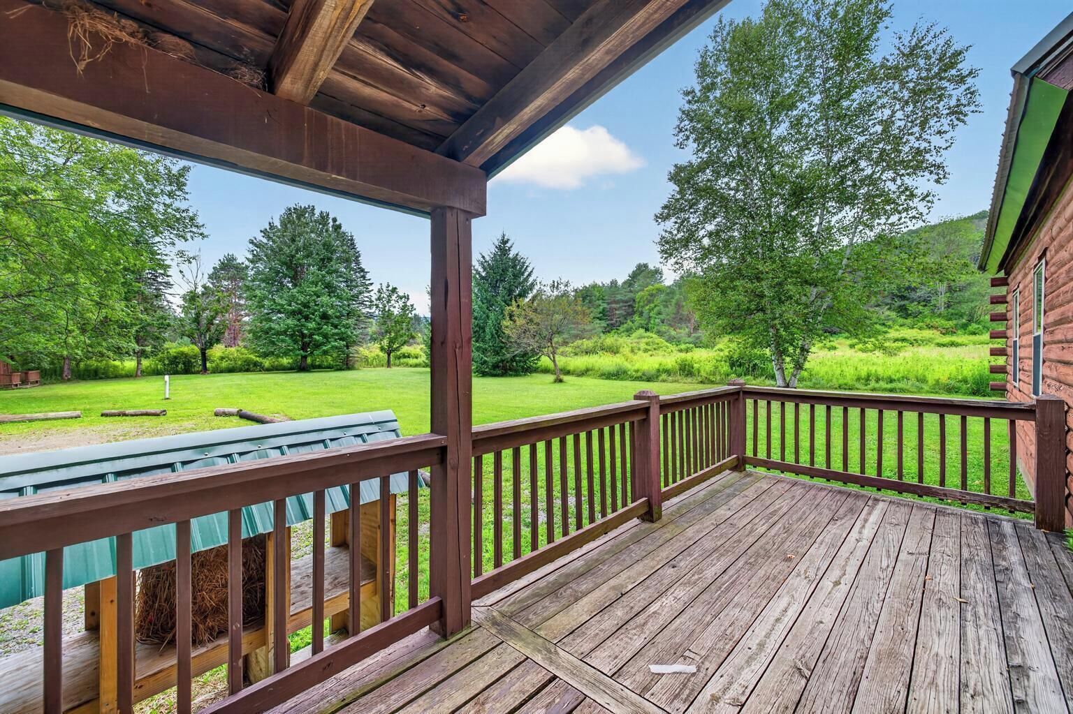 A wooden deck with a railing, a picnic table, and a view of a green landscape with trees.