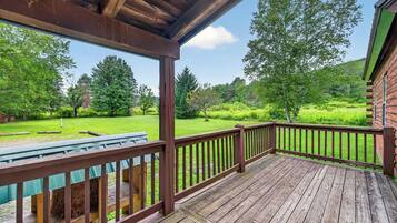 A wooden deck with a railing, a picnic table, and a view of a green landscape with trees.