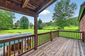 Una terraza de madera con barandilla, una mesa de picnic y vistas a un paisaje verde con árboles.