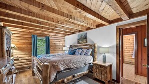A wooden cabin bedroom with a bed, nightstand, and a view of the outdoors. - 1/2 mile to EVL, Lake, HOT TUB, Pets welcome (Ellicottville)