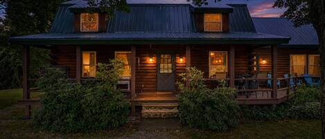 A log cabin with a porch, multiple windows, and a well-lit entrance.