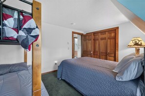 Un dormitorio con una cama litera, una cama individual, un armario de madera y una lámpara.