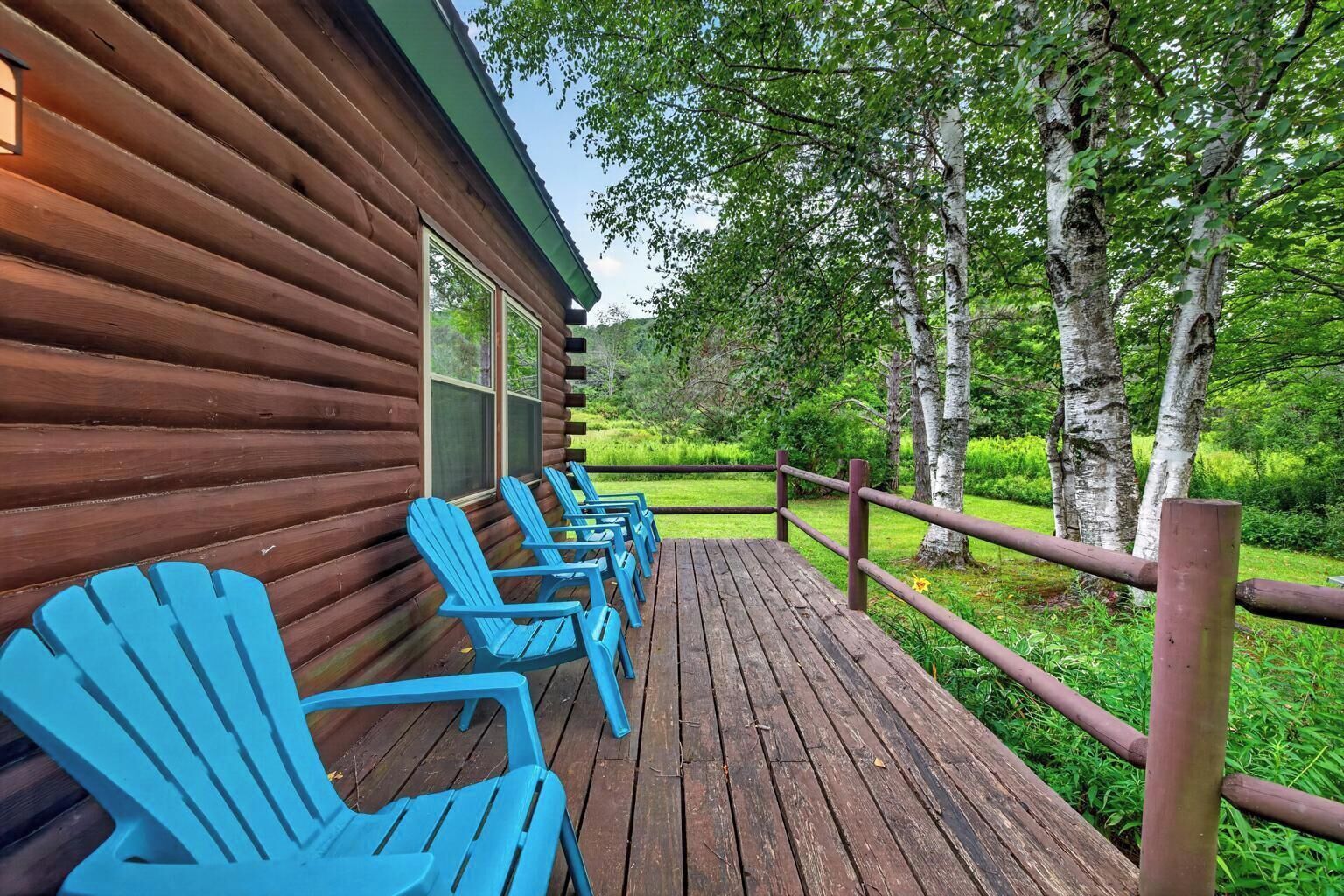 A wooden cabin with a deck and blue Adirondack chairs.