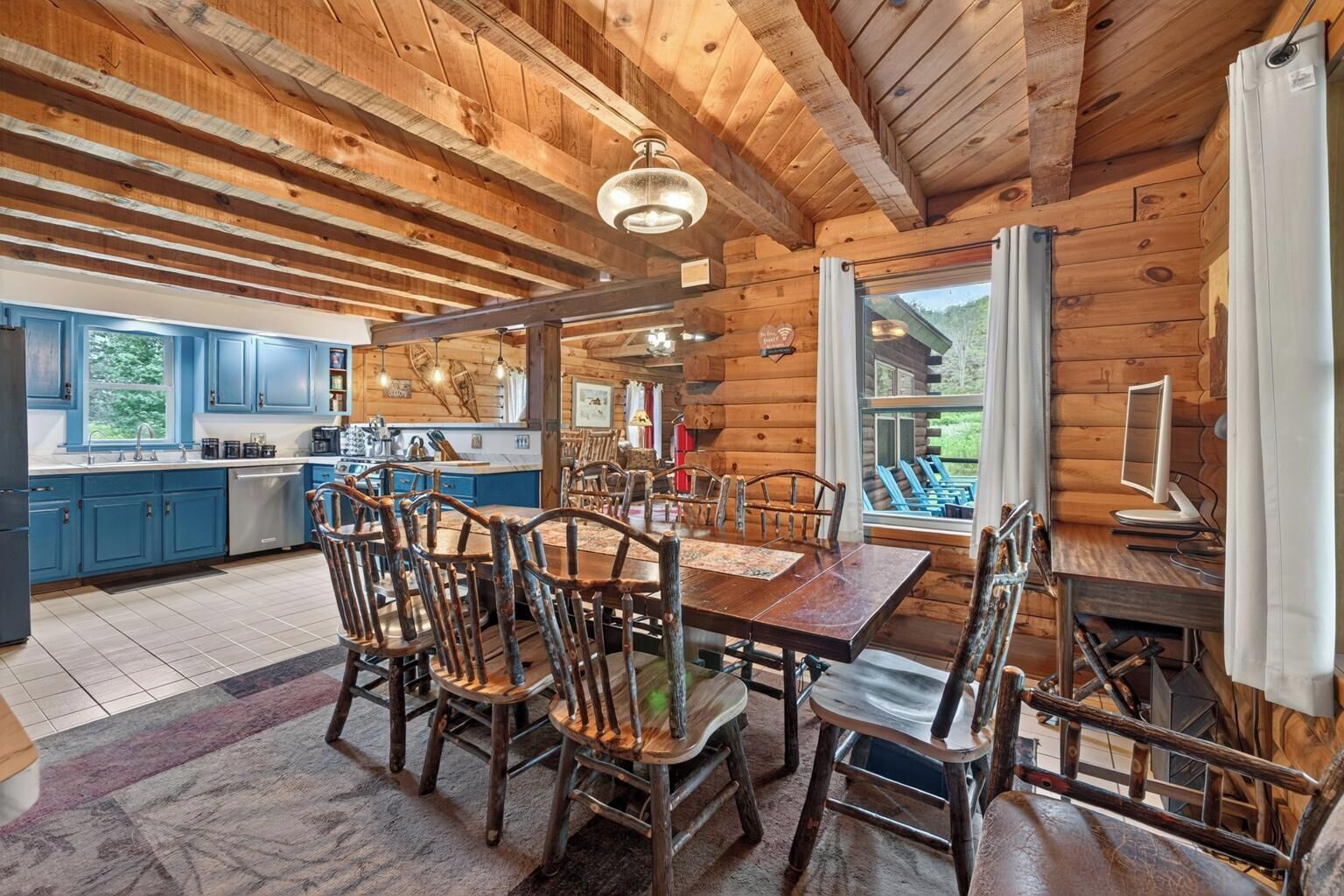 L’intérieur d’un chalet rustique comprend une table à manger en bois, des chaises, un coin cuisine et une grande fenêtre donnant sur un paysage pittoresque.