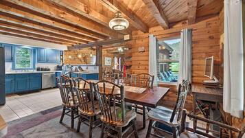 L’intérieur d’un chalet rustique comprend une table à manger en bois, des chaises, un coin cuisine et une grande fenêtre donnant sur un paysage pittoresque.