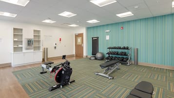 A fitness center with exercise equipment, a wall-mounted dumbbell rack, and a wall-mounted scale.