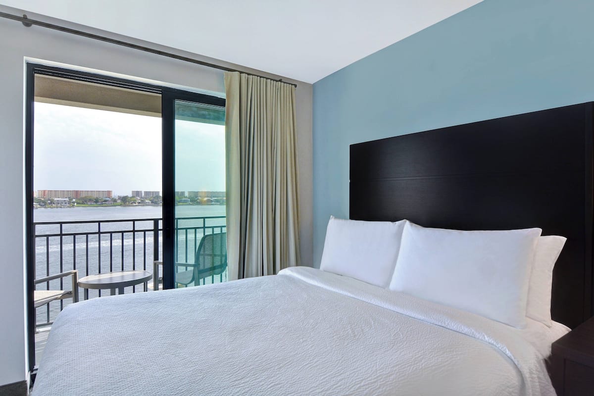 Ein Hotelzimmer mit einem großen Bett, einem Balkon mit Blick auf das Wasser und einem Tisch mit Stuhl auf dem Balkon.