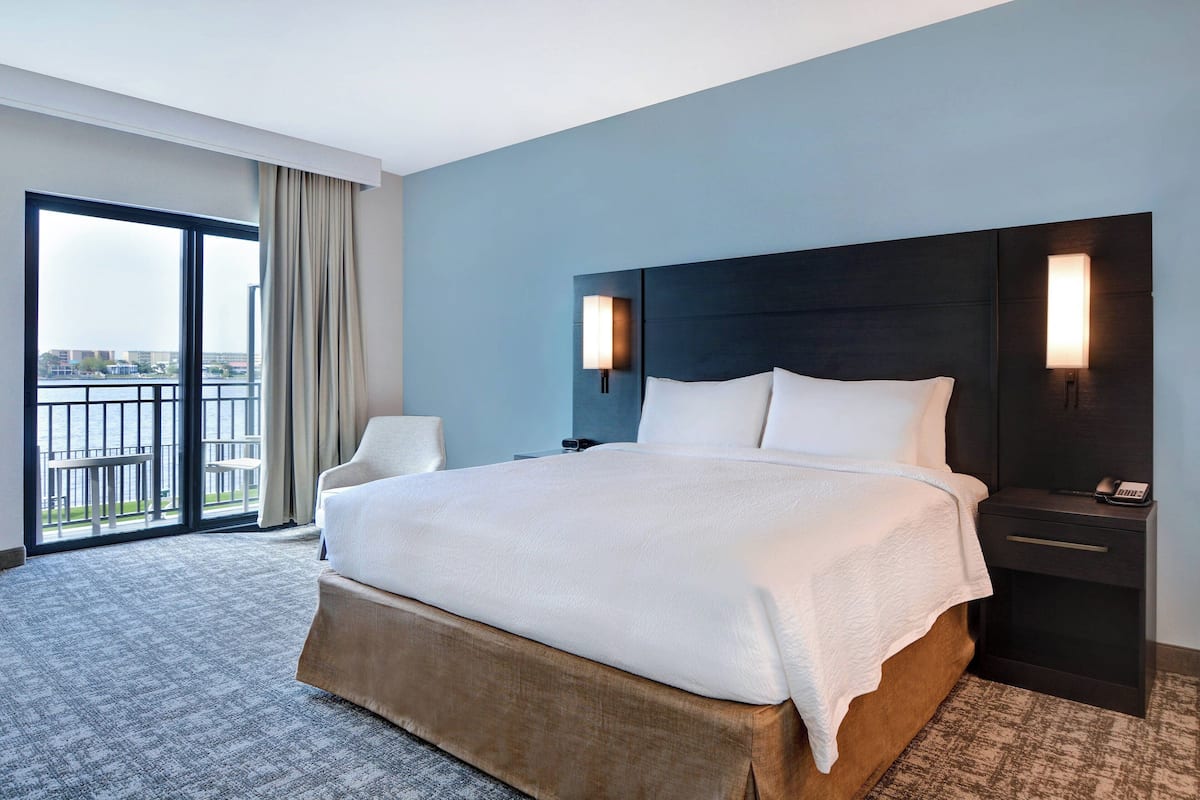 Ein Hotelzimmer mit einem großen Bett, einem Nachttisch, einem Sessel und Blick ins Freie.